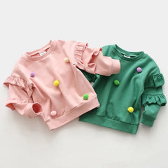 Girls Pom Pom Jumper in pink and green, available in sizes 2-10 years from Bijou Bubs, featuring colorful pom poms and ruffled sleeves.